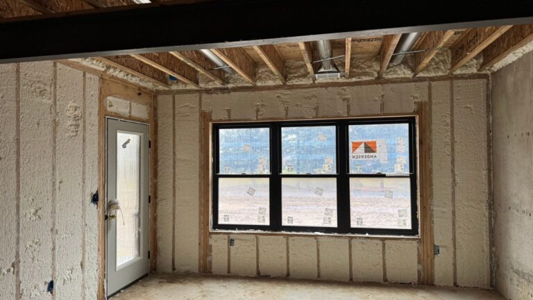 Room in a new home with spray foam insulation between the wall studs around a window